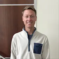 Professional headshot of Austin Cook, a smiling man wearing a white quarter-zip pullover.