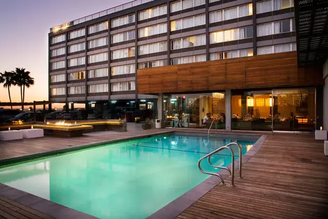 Modern hotel exterior featuring a lit swimming pool and outdoor lounge at dusk.