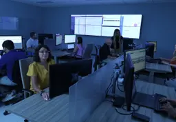 Team of people working at computers in a modern operations center with large wall displays.