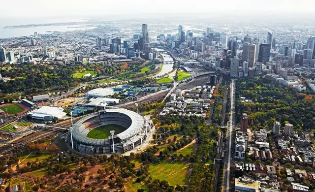 Aerial view of a large sports stadium and surrounding parkland in a major city.