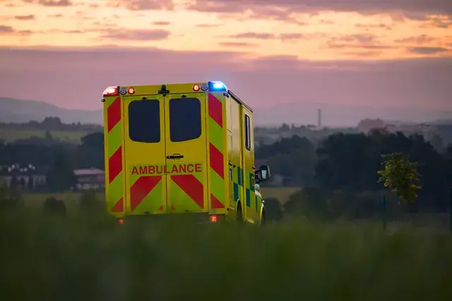Rear view of an ambulance with flashing lights driving through a rural landscape at sunset.